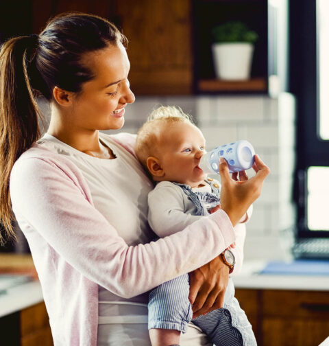 Glückliche Mutter, die ihr Baby in der Küche mit Babyflasche füttert