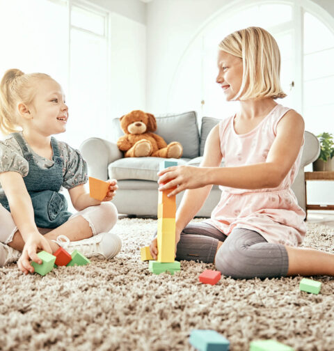 2 Mädchen spielen mit Kinder-Spielzeug, das auf dem Boden unordentlich liegt