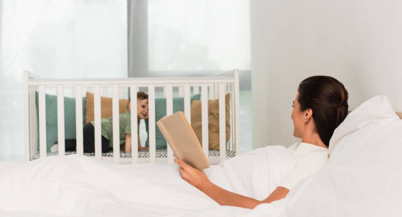 Elternteil schaut zu Beistellbett neben dem Bett