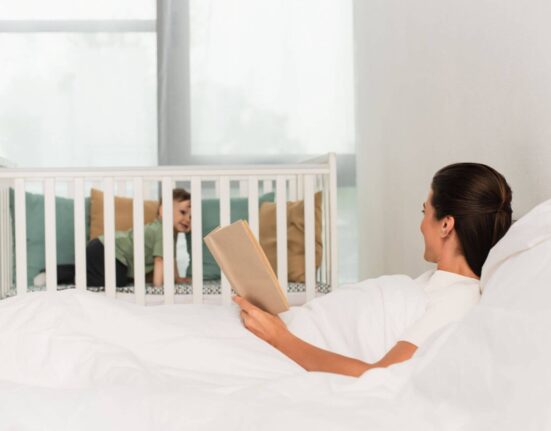 Elternteil schaut zu Beistellbett neben dem Bett