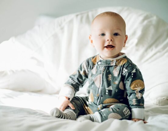 Baby mit Strampler auf dem Bett