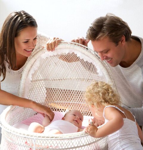 Familie steht um Stubenwagen mit Baby