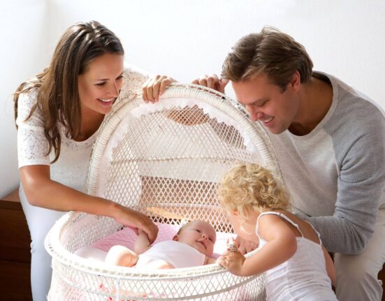 Familie steht um Stubenwagen mit Baby